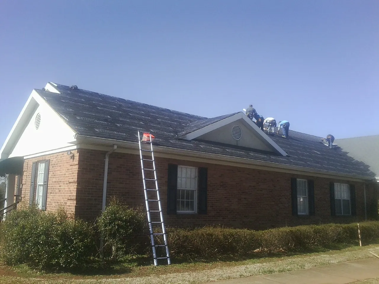 Crew tearing shingles off a brick ranch roof with a ladder set — Metal Roof Repair work by our crew in Kansas City