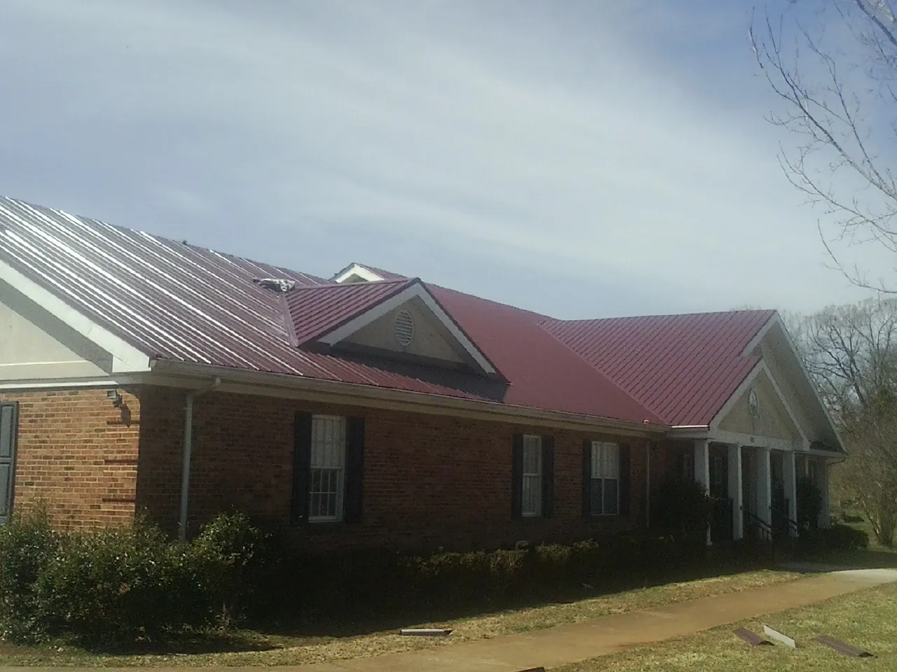Red metal roof with gabled entries on a long brick building, from a Hail Damage Roof Repair job in Kansas City